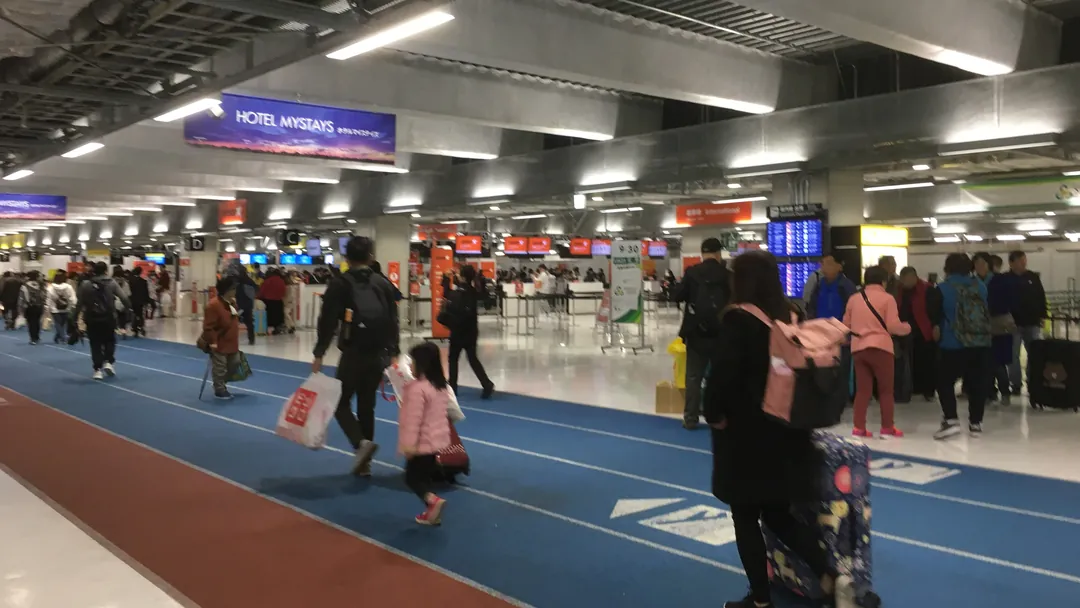 나리타 공항 제3터미널 로비에서 캐리어와 쇼핑백을 들고 걷는 여행객들 사진