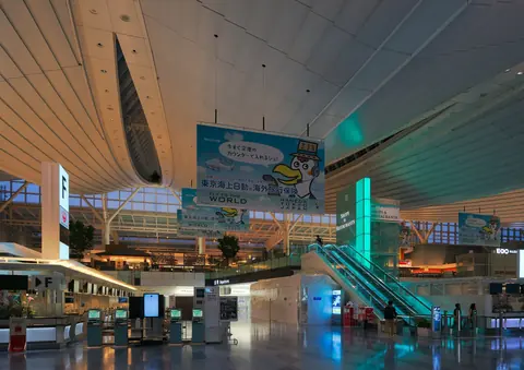 The departure lobby of Haneda Airport's international terminal in the evening, with check-in counters and escalators.