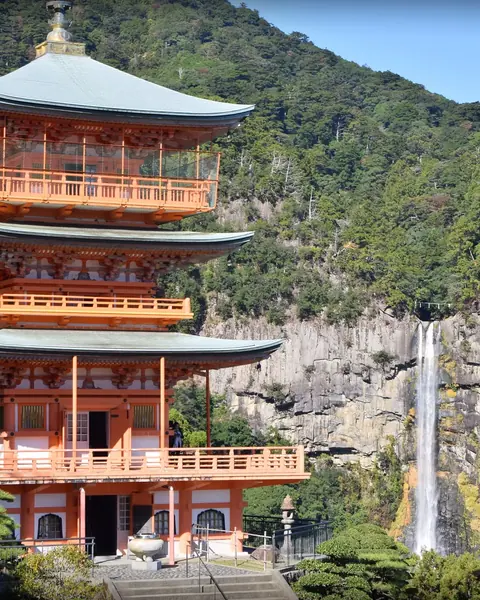The vermilion three-story pagoda of Seiganto-ji in front of Nachi Falls and forested mountains in Wakayama.