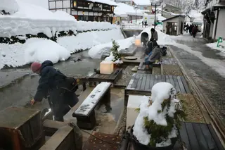 Visitors at the snowy riverside footbath in Ginzan Onsen, Yamagata.
