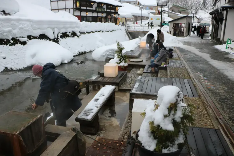 Visitors at the snowy riverside footbath in Ginzan Onsen, Yamagata.