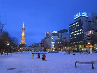 Snow-covered Odori Park in Sapporo at dusk, with the lit Sapporo TV Tower at the far end.
