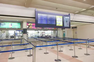 Empty queue lanes in front of the security check at Kochi Airport, below a flight information screen.