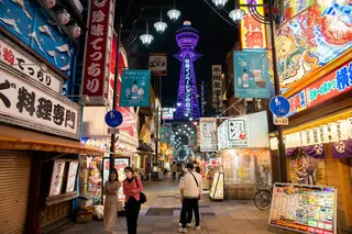 Shinsekai's neon-lit shopping street in Osaka at night, with the purple-lit Tsutenkaku Tower at the end.