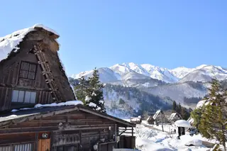 Snow-covered gassho-zukuri farmhouses in Shirakawa-go with white mountains under a clear winter sky.