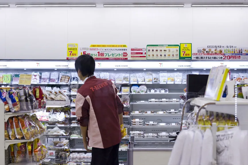 Interior of a 7-Eleven convenience store in Japan with a staff member stocking shelves