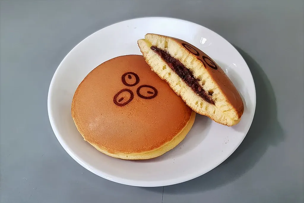 A dorayaki pancake cut open showing red bean paste filling, beside a whole dorayaki on a plate