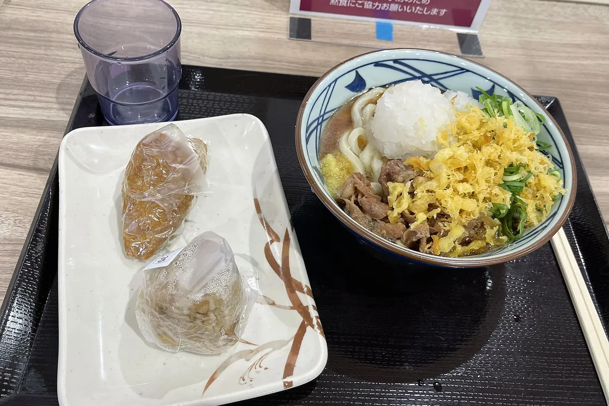 盘子里的稻荷寿司，旁边是一碗加了萝卜泥、葱花和天妇罗碎的牛肉乌冬面
