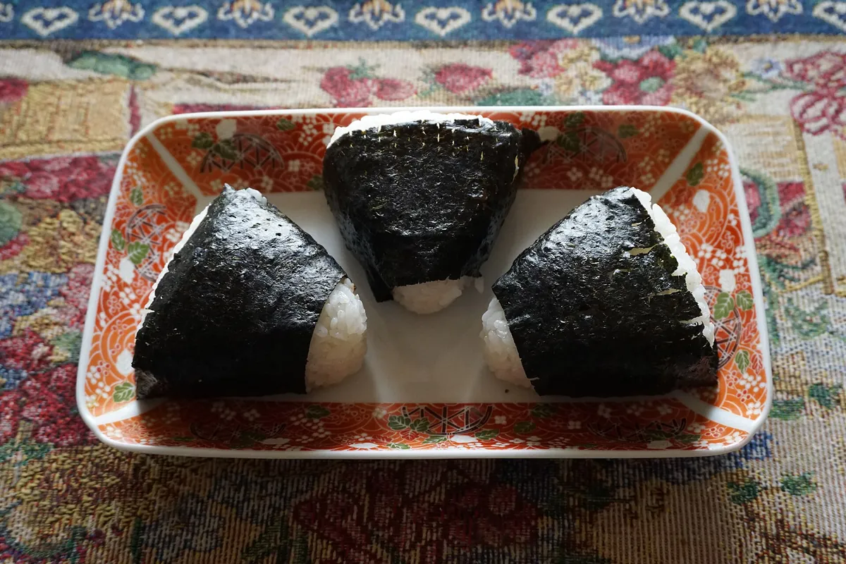 Three triangular onigiri rice balls wrapped in nori seaweed on a patterned orange plate