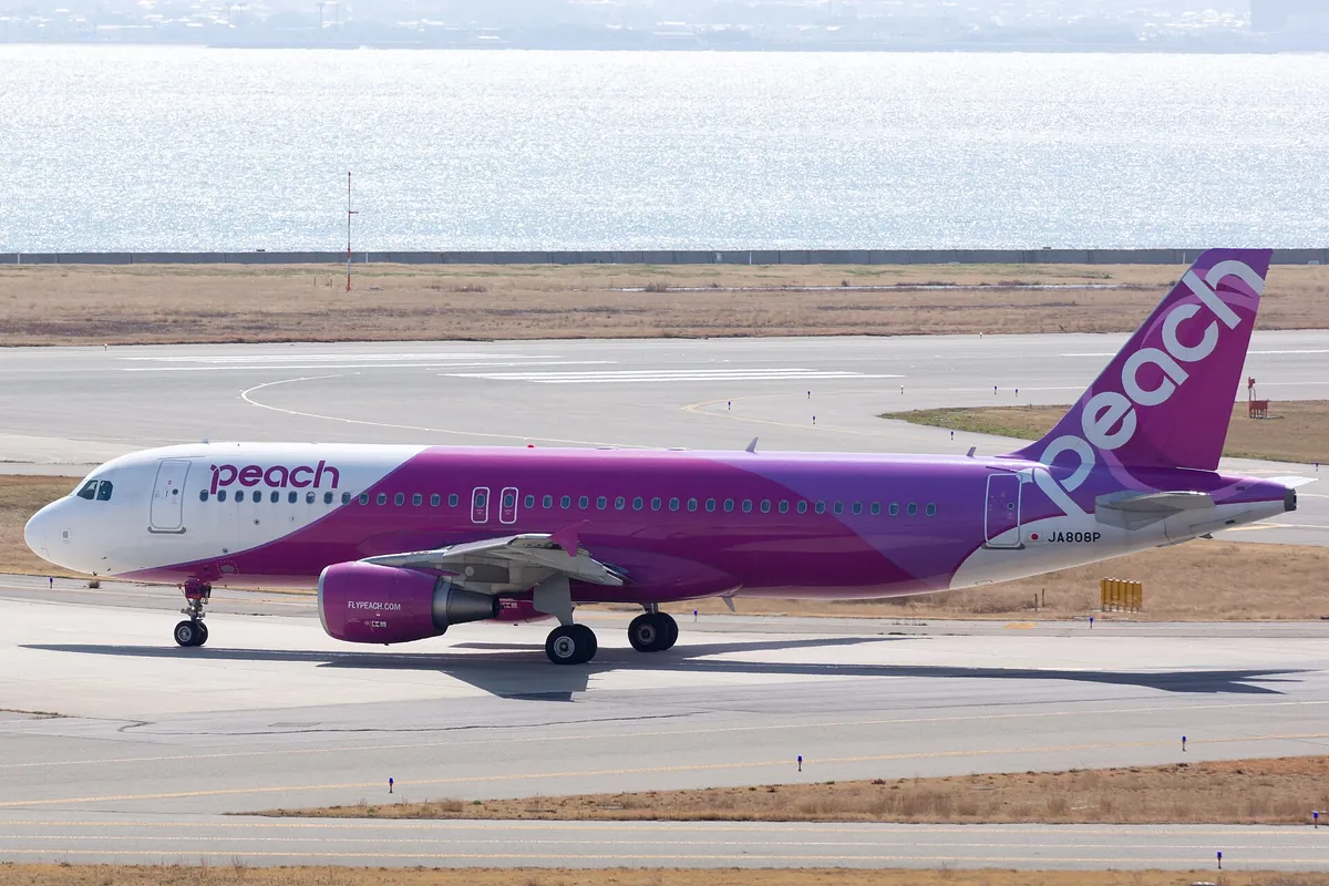 A pink and white Peach Aviation Airbus A320 on the taxiway with the sea visible in the background