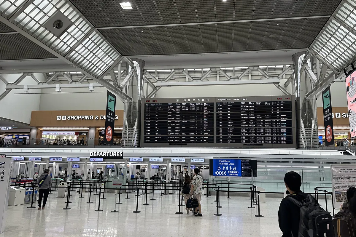 Travelers standing before a departures information board and check-in counters in an airport terminal