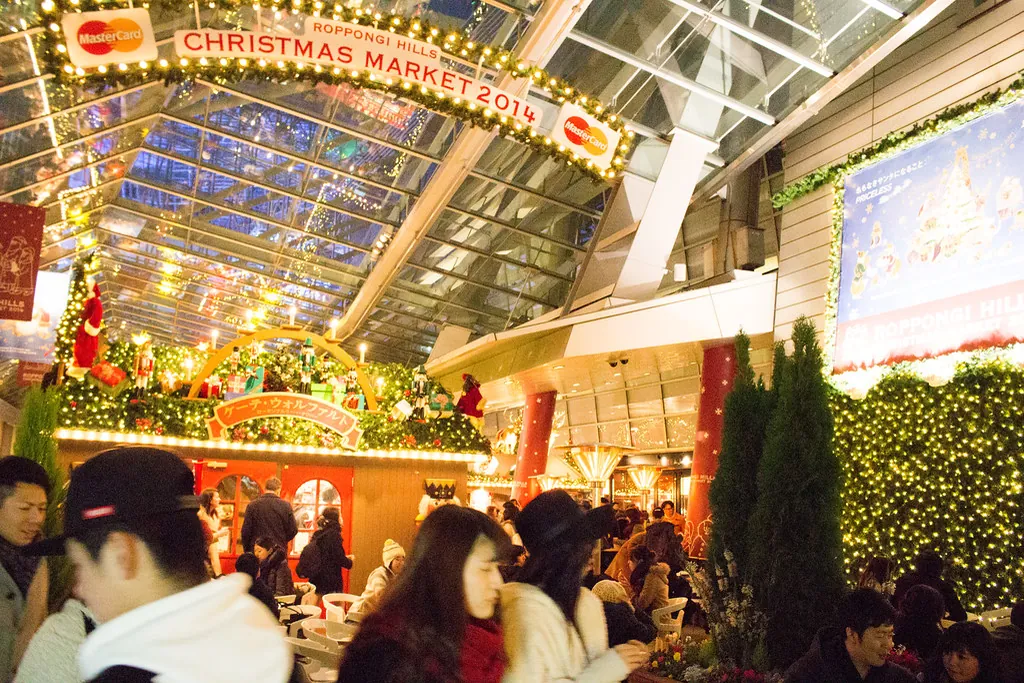 六本木之丘玻璃屋頂下亮著燈的聖誕市集攤位，掛著 Christmas Market 2014 的布條