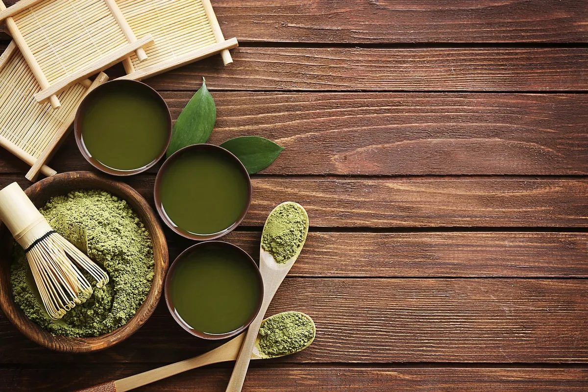 深色木桌上放着三碗绿色抹茶、一把竹茶筅、一碗抹茶粉和几把木勺
