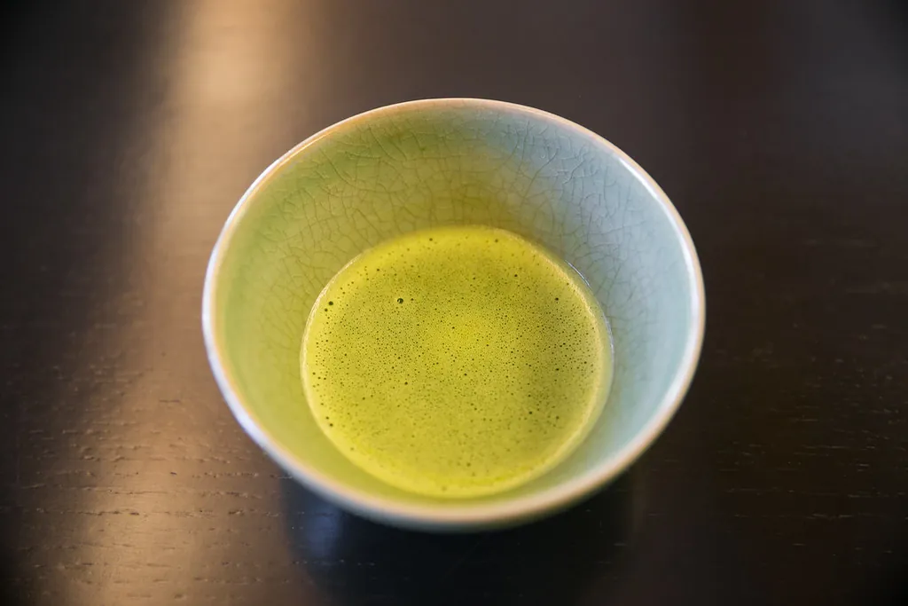 深色木桌上，一只冰裂釉茶碗里盛着起泡的浅绿色抹茶