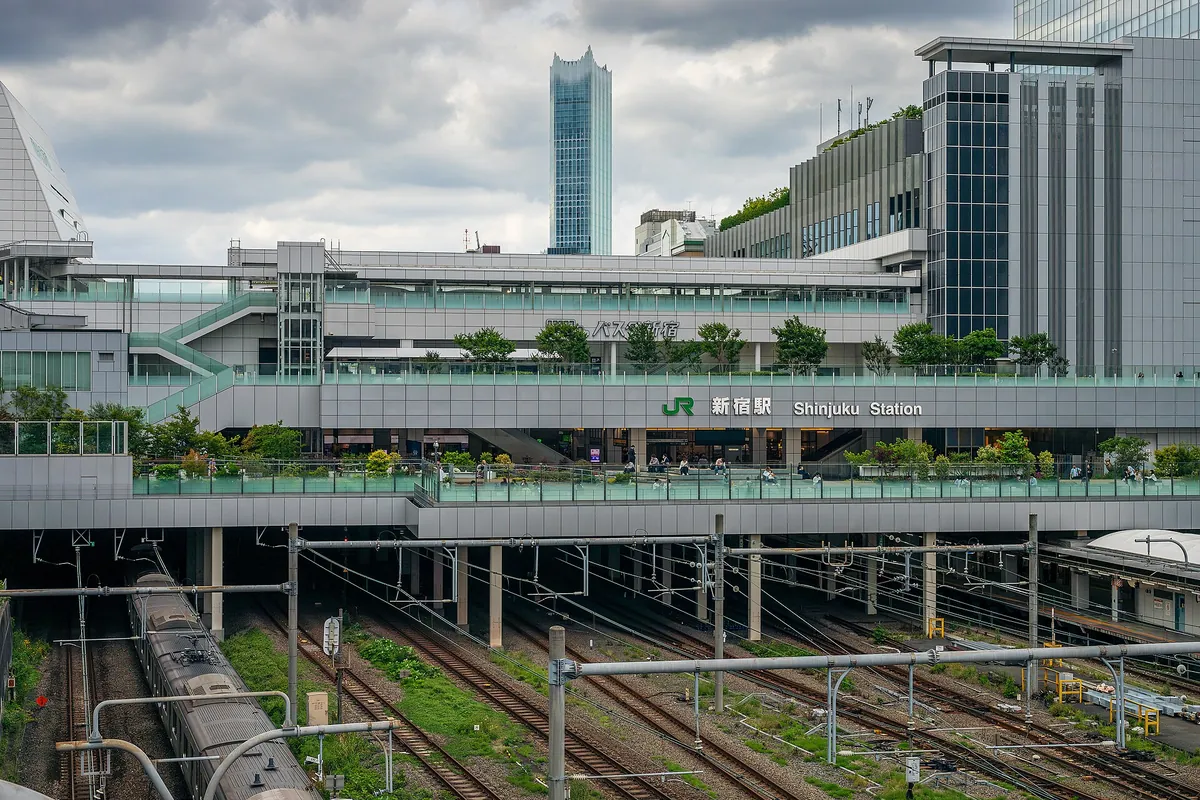 铁轨和站台上方建筑上的JR新宿站标识，后方是摩天大楼