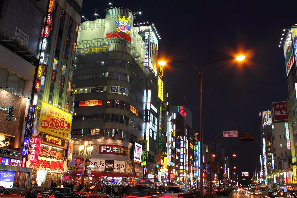 新宿歌舞伎町夜晚霓虹闪烁的街道，有亮灯的招牌、唐吉诃德大楼和来往车辆