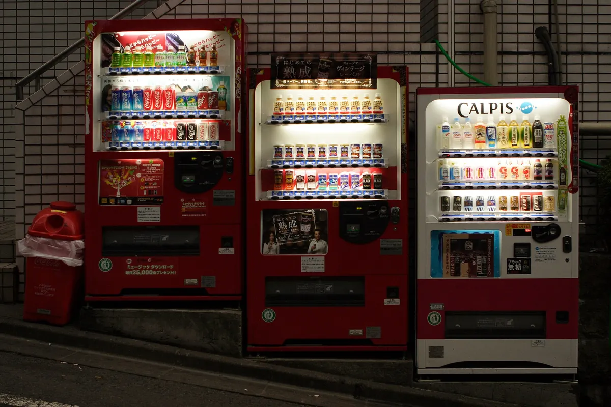 夜の日本の街にある、缶や瓶の飲料が入った自動販売機3台