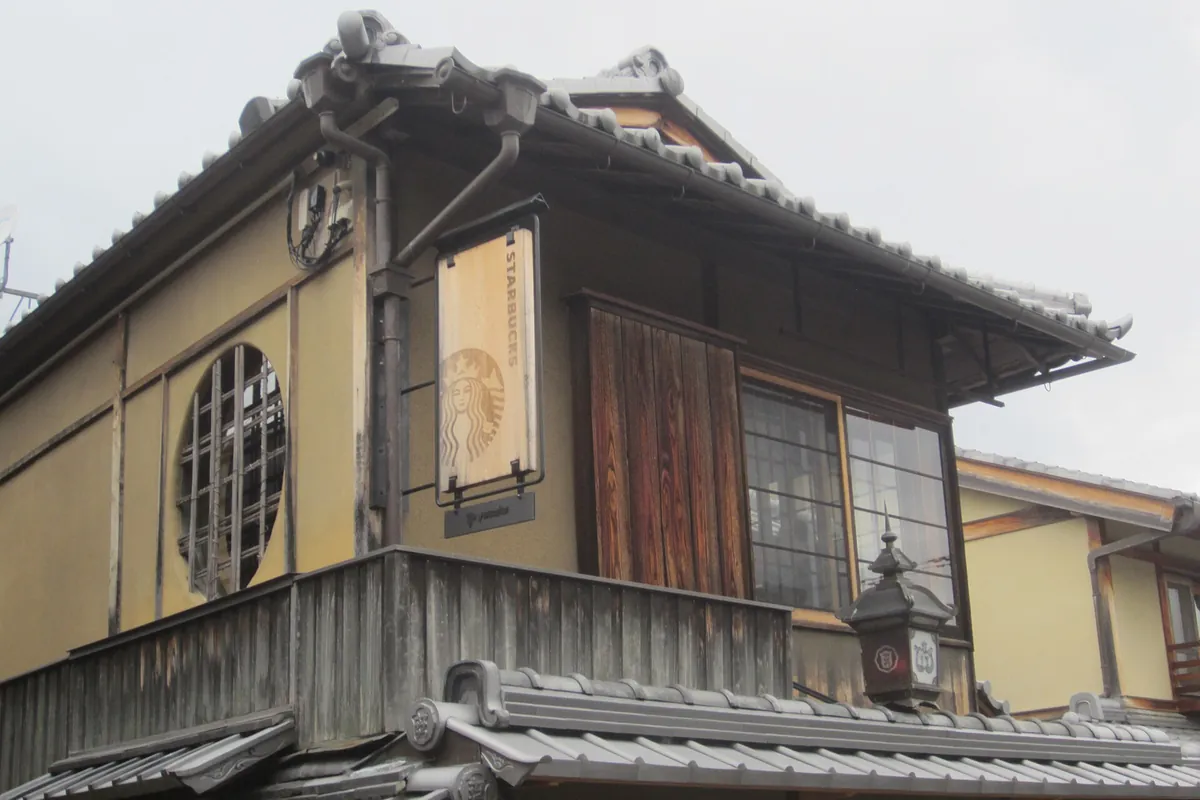 京都にある、瓦屋根と丸窓のある木造の町家に掲げられたスターバックスの看板