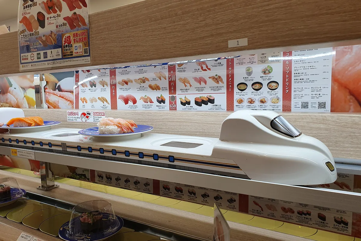 日本の回転寿司店でメインのレーンの上を新幹線型のレーンカーが寿司の皿を運んでいる様子