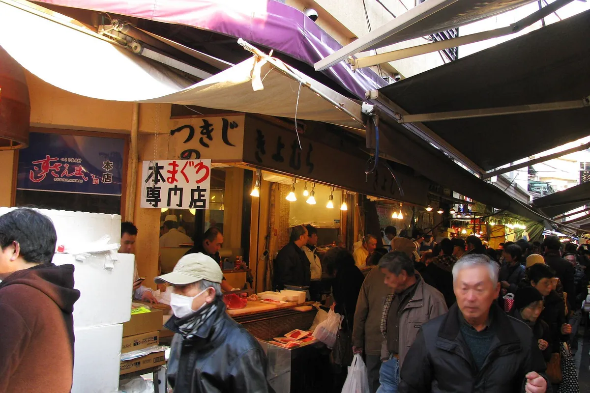 東京・築地場外市場の通りで、海産物の屋台や店の看板の前を歩く買い物客たち
