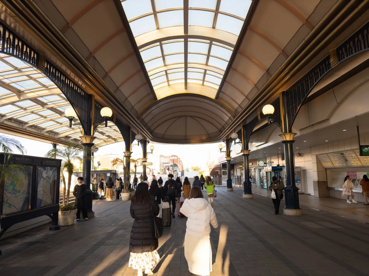 Glass-roofed concourse outside JR Maihama Station with visitors walking