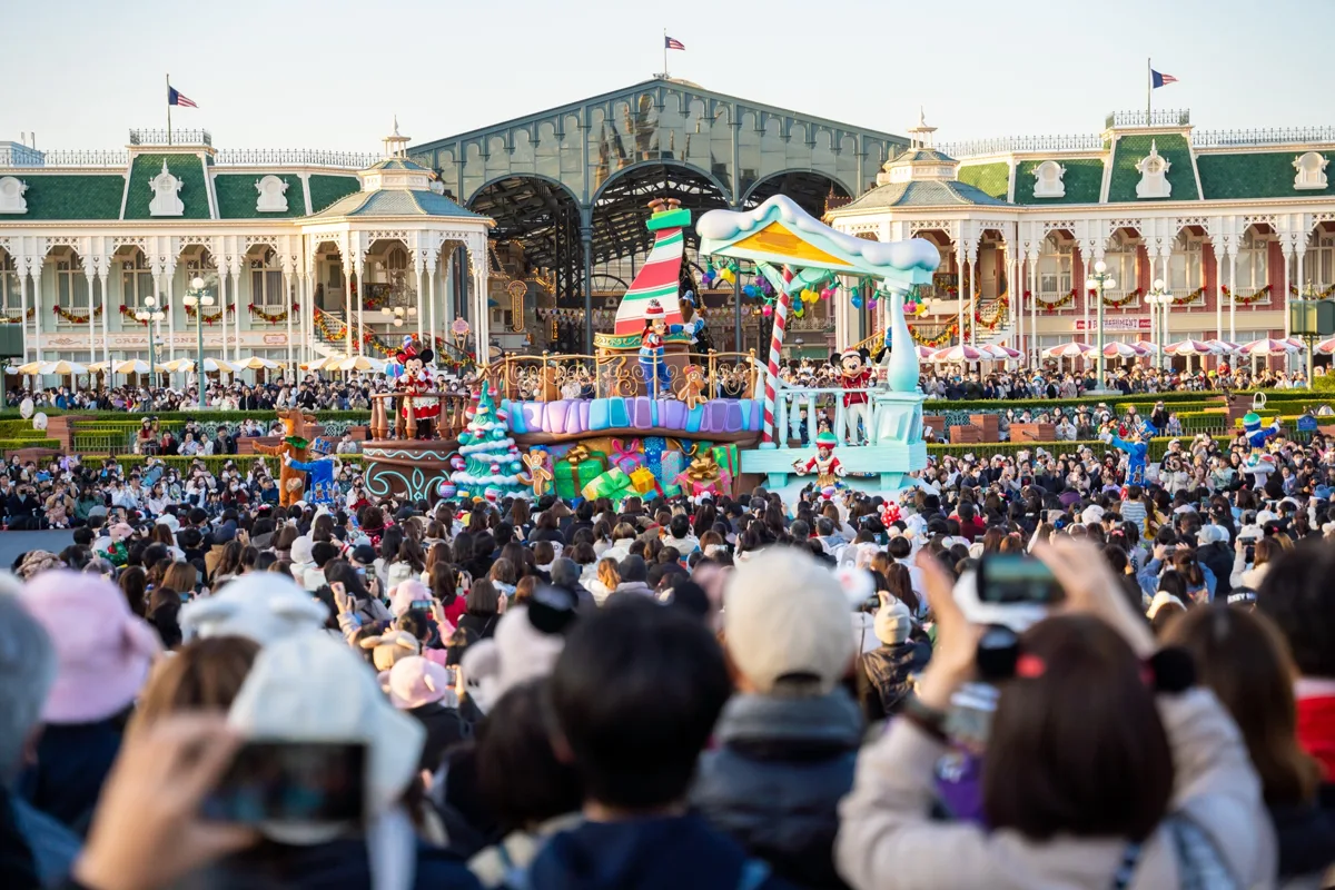 Dense crowd holding up phones to watch a daytime parade float in front of the World Bazaar buildings