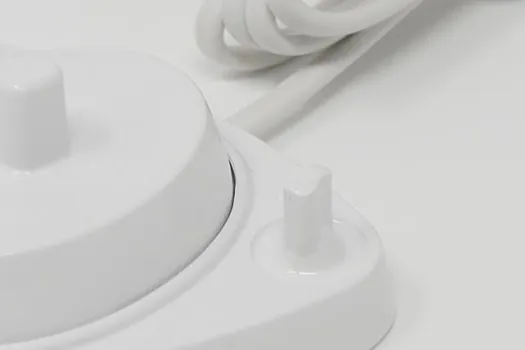 丸くて白い充電台に出っ張ったピンとコイル状の白い電源コードが付いているクローズアップ