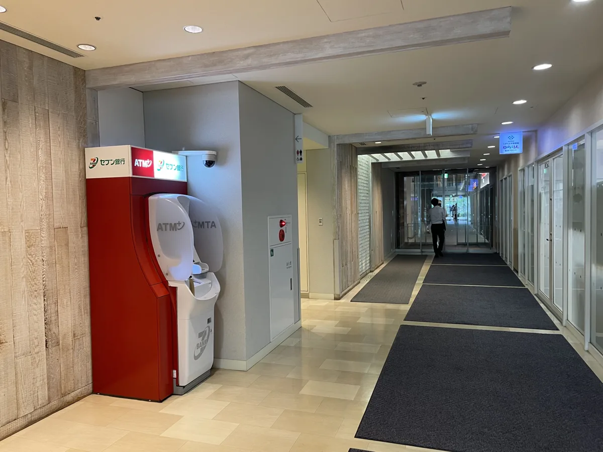 A red and white Seven Bank ATM in a corridor of a Tokyo office building, photographed in July 2025