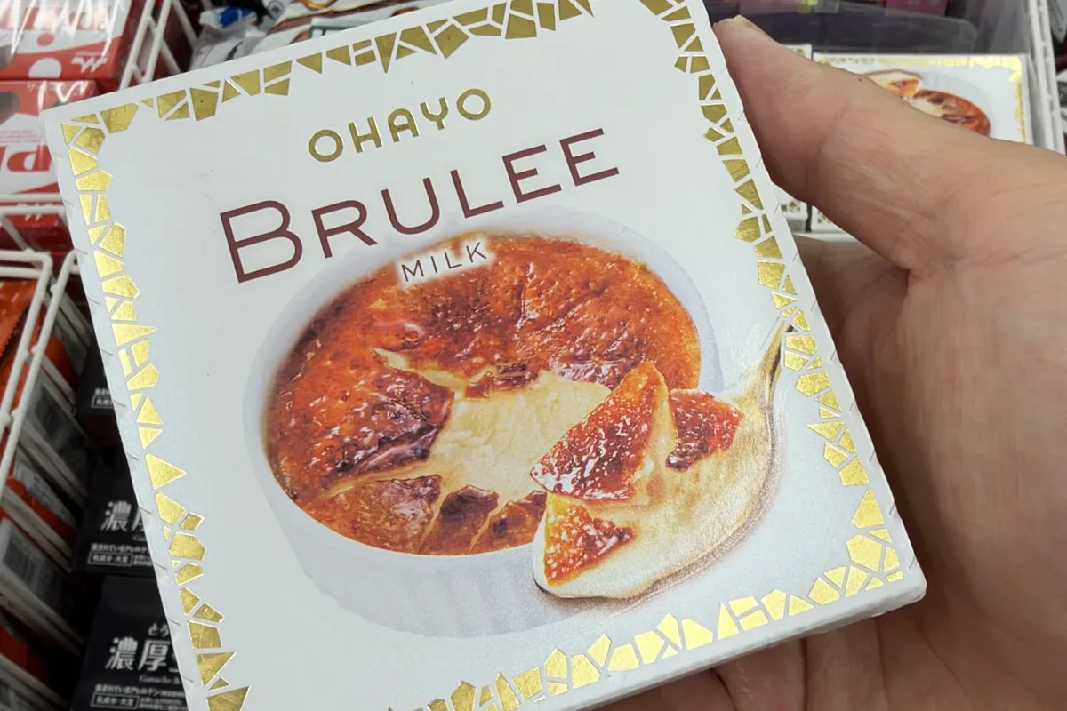 東京のセブン-イレブンの冷凍ケースの前で掲げられたオハヨー ブリュレミルクアイスクリームの箱