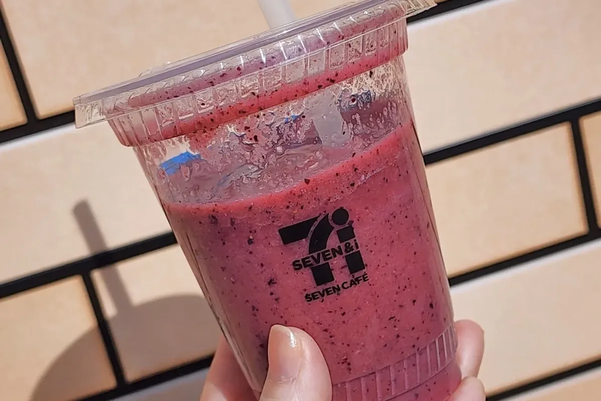 A Seven Cafe frozen smoothie in a clear plastic cup with a straw, held in a hand