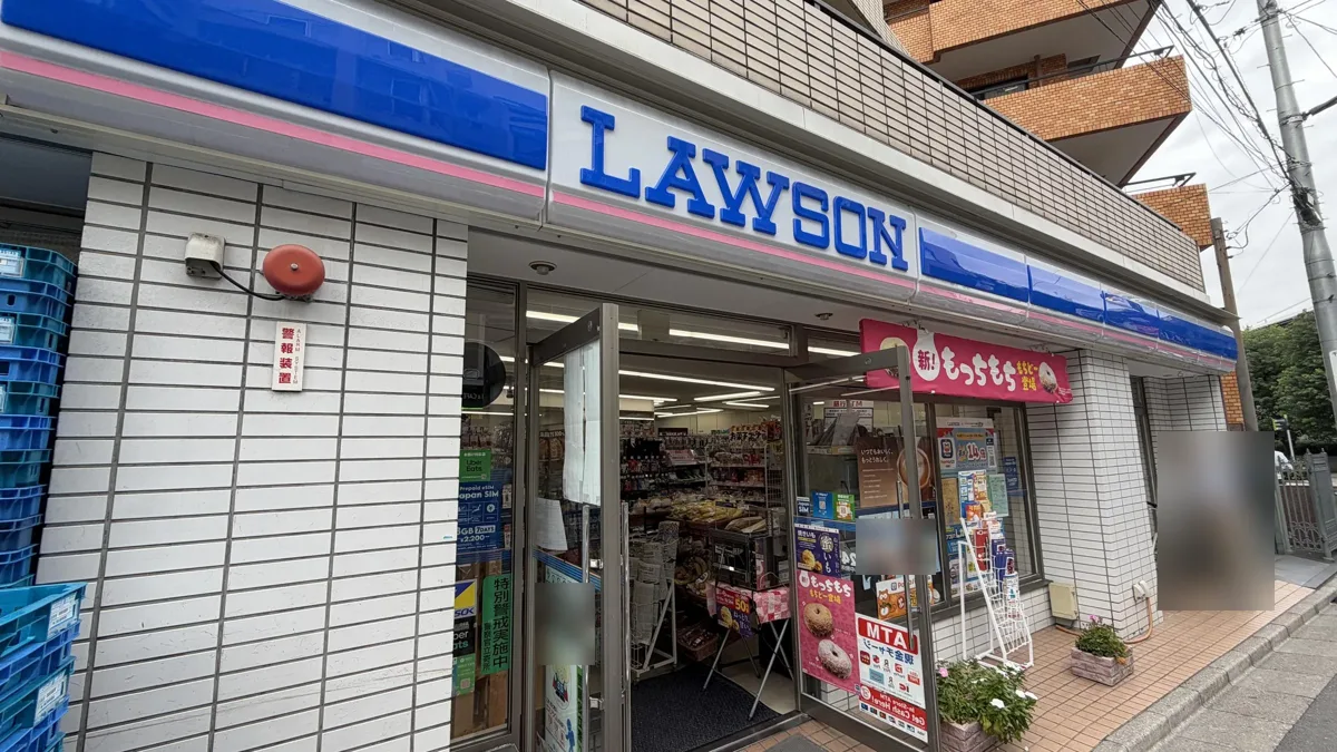 The front of a Lawson store in Tokyo, with the blue LAWSON sign over the glass doors and posters by the entrance