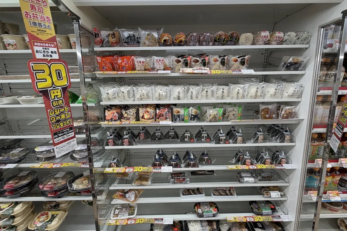 A 7-Eleven onigiri shelf in a Tokyo store on 20 October 2026, with sushi rolls and bento on the lower rows