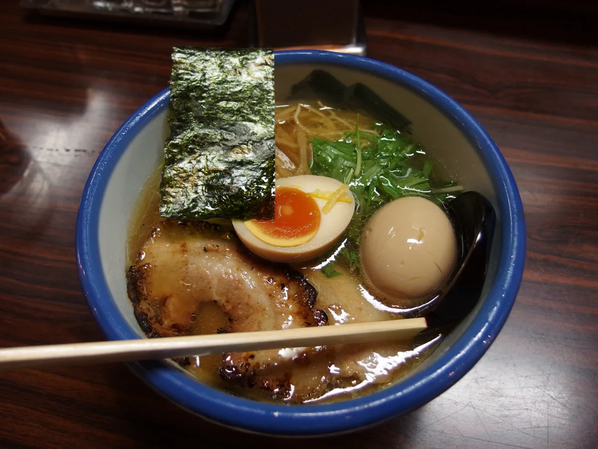 A bowl of AFURI ramen with a sheet of nori, sliced pork, soft-boiled eggs and greens