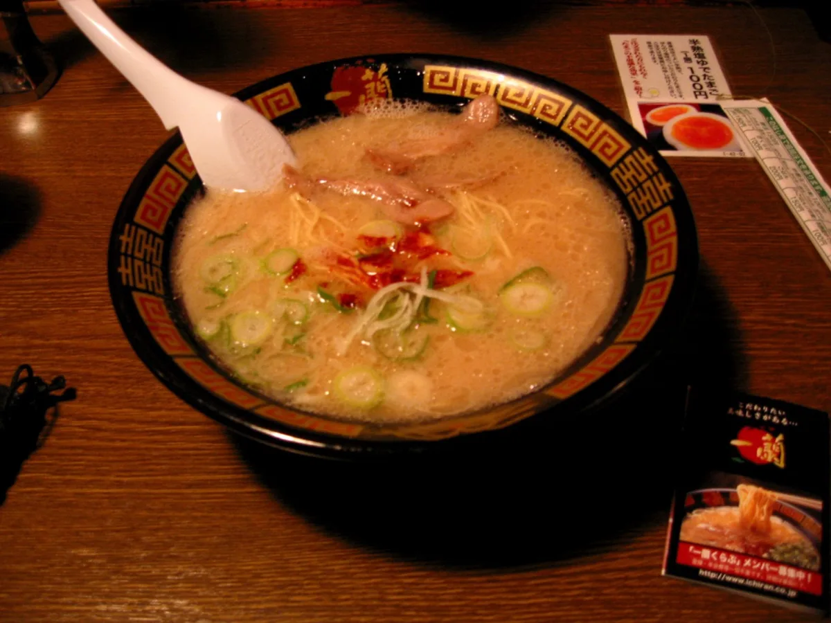 木製吧台上的一碗 Ichiran 豚骨拉麵，配有叉燒、蔥和紅色辣醬