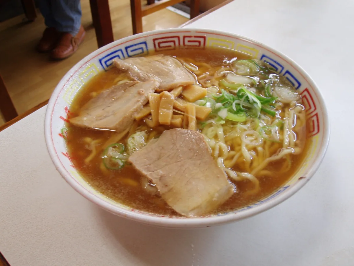 A bowl of Kitakata ramen with soy sauce broth, wavy noodles, sliced pork, bamboo shoots and green onions