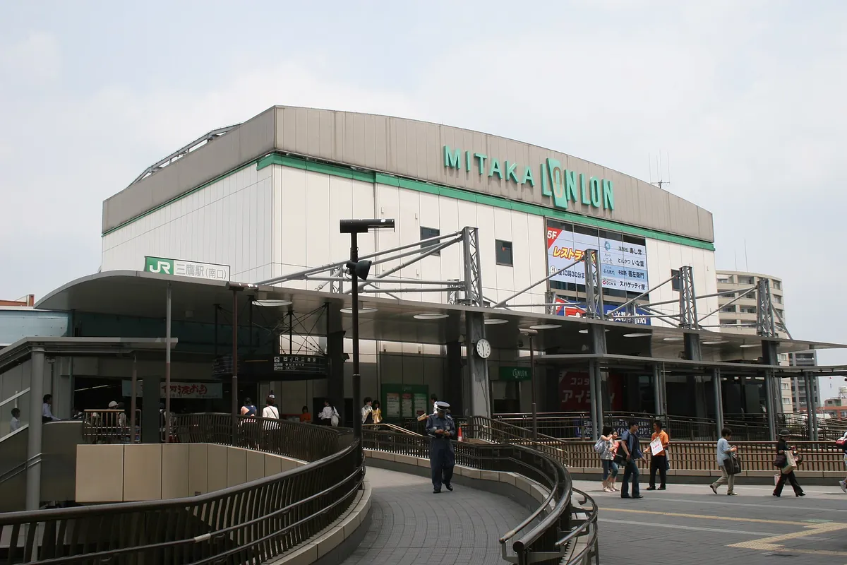 The Mitaka Lonlon building at JR Mitaka Station in Tokyo, with pedestrians and a staff member on the curved walkway outside.