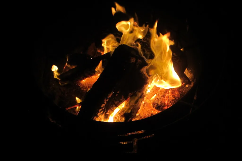 Burning logs and flames inside a round metal fire pit at night