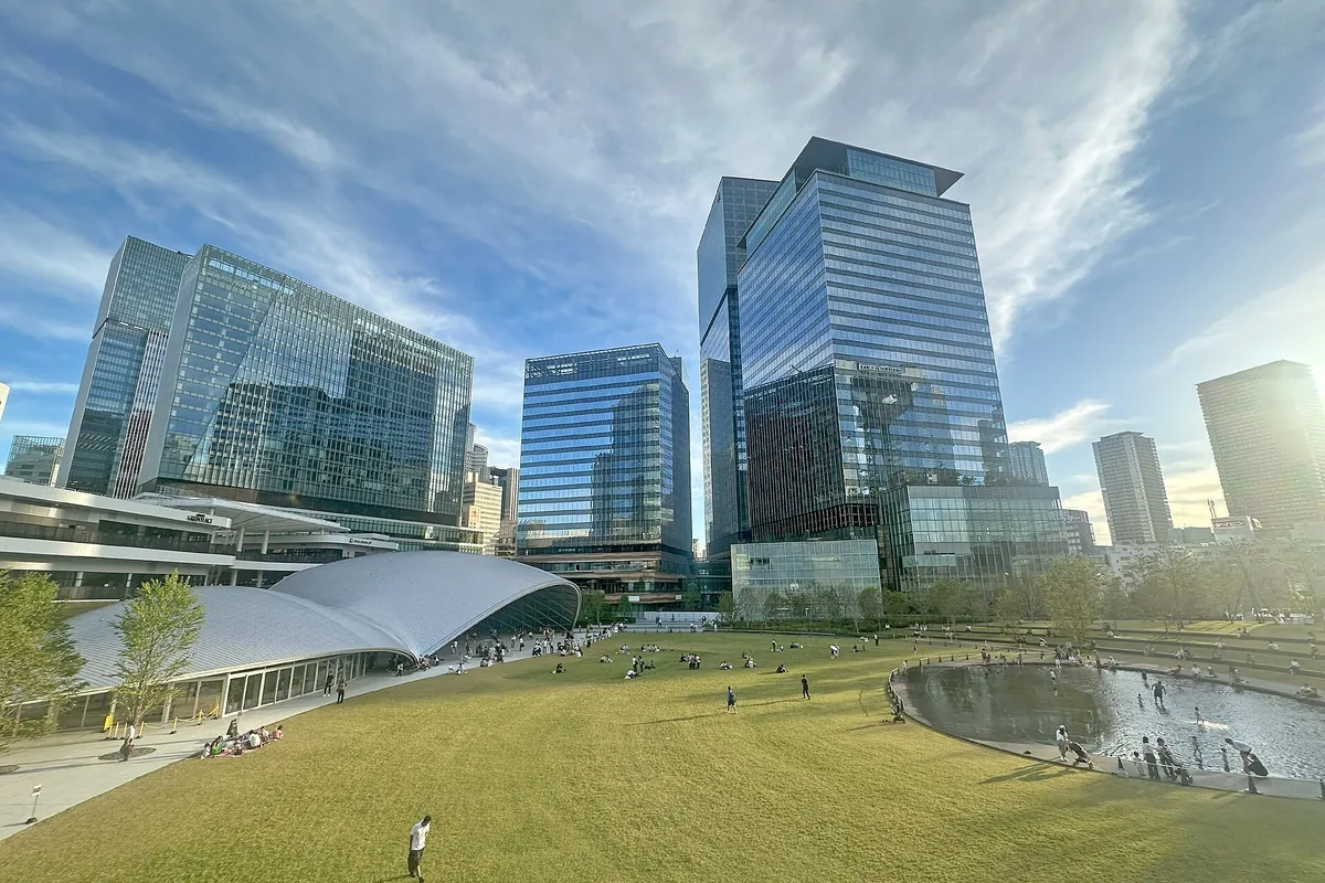 Lawn and trees in a park with the glass skyscrapers of Grand Green Osaka rising behind
