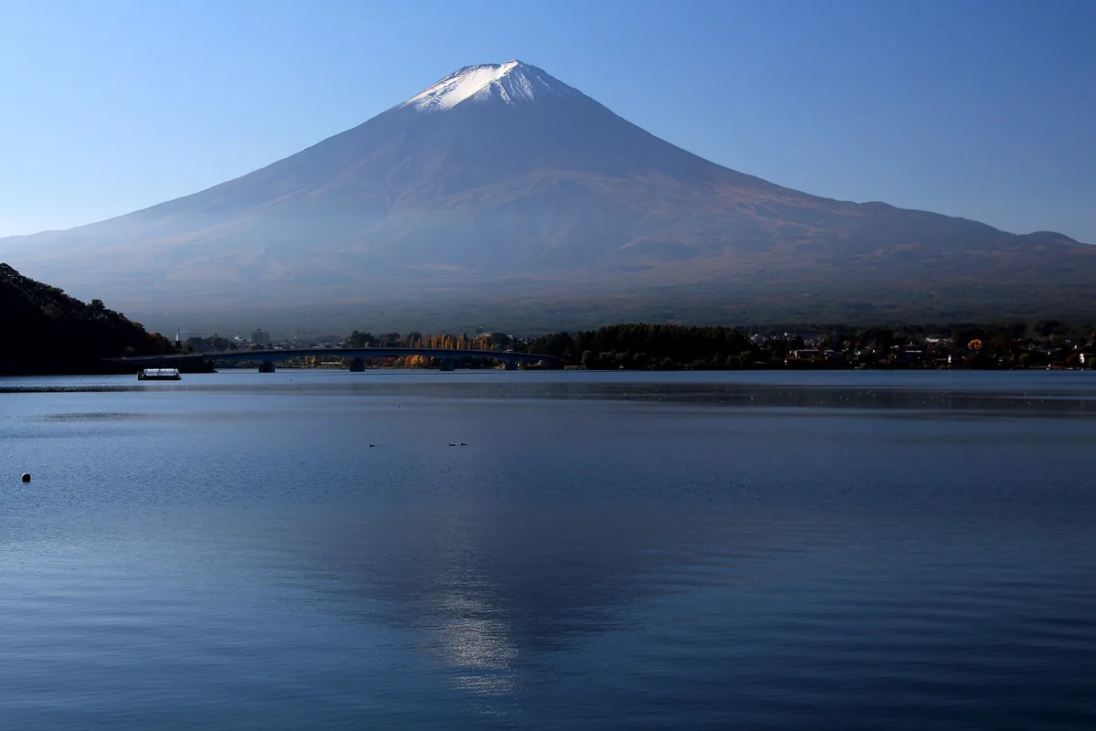 Snow-capped Mount Fuji rising above Lake Kawaguchi in Yamanashi, with a small boat on the lake