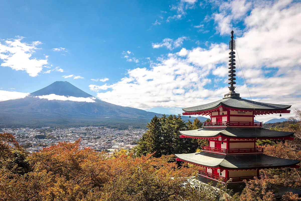 The red five-story Chureito Pagoda with snow-capped Mount Fuji rising behind it, surrounded by autumn trees in Yamanashi