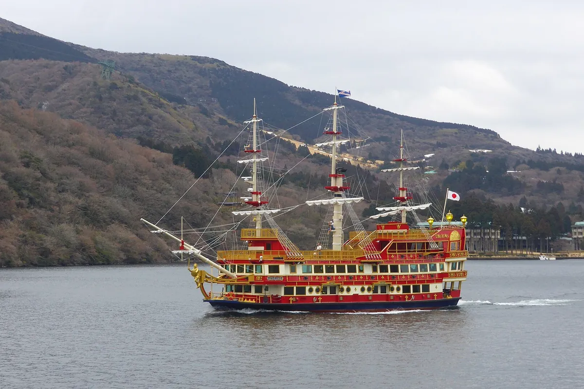 A red and gold pirate-themed sightseeing ship sailing on Lake Ashi in Hakone with mountains in the background