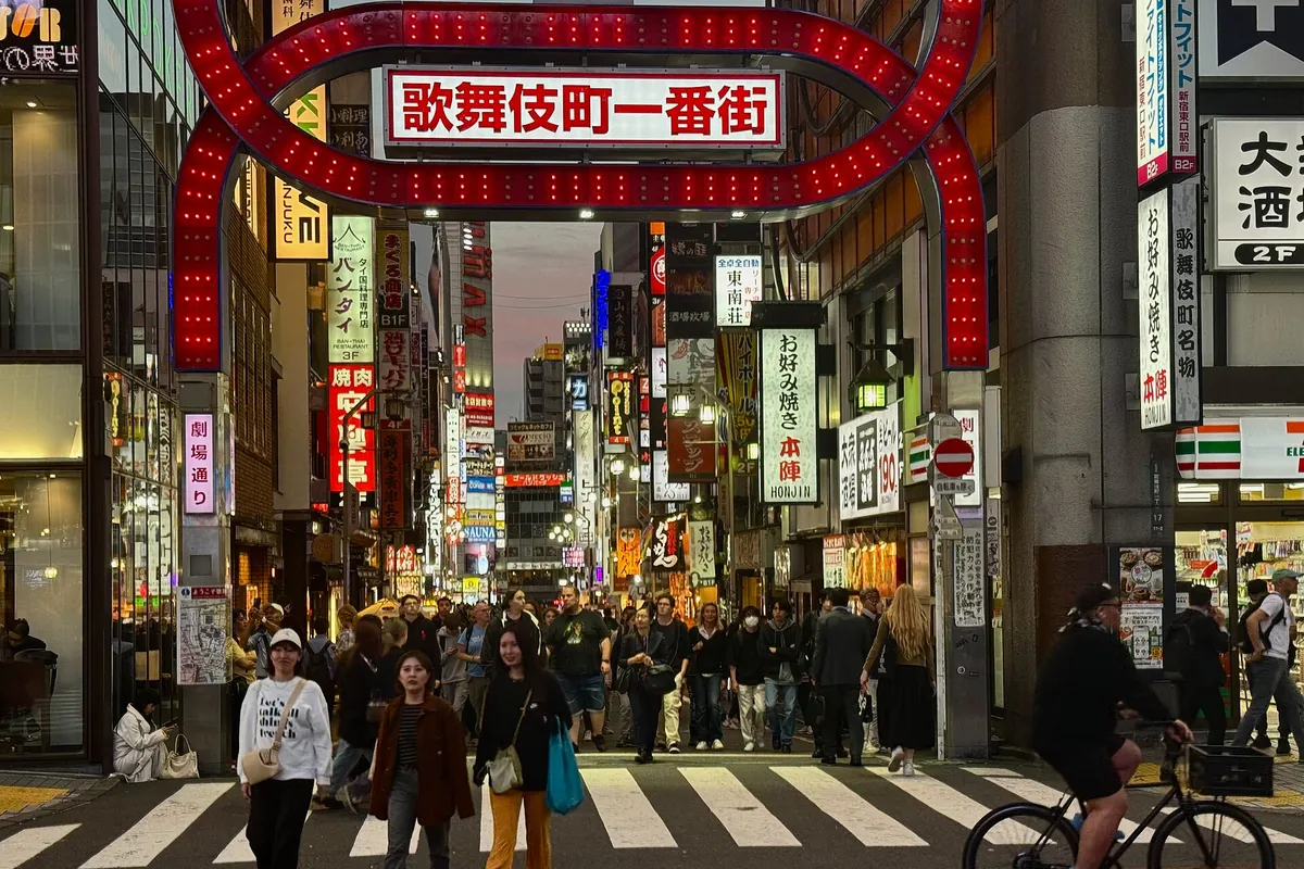 The red neon Kabukicho Ichiban-gai gate arching over a street crowded with pedestrians in Shinjuku, Tokyo