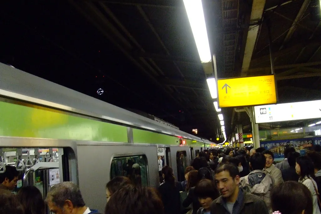 A green JR Yamanote Line train stopped at a crowded platform with passengers boarding at night