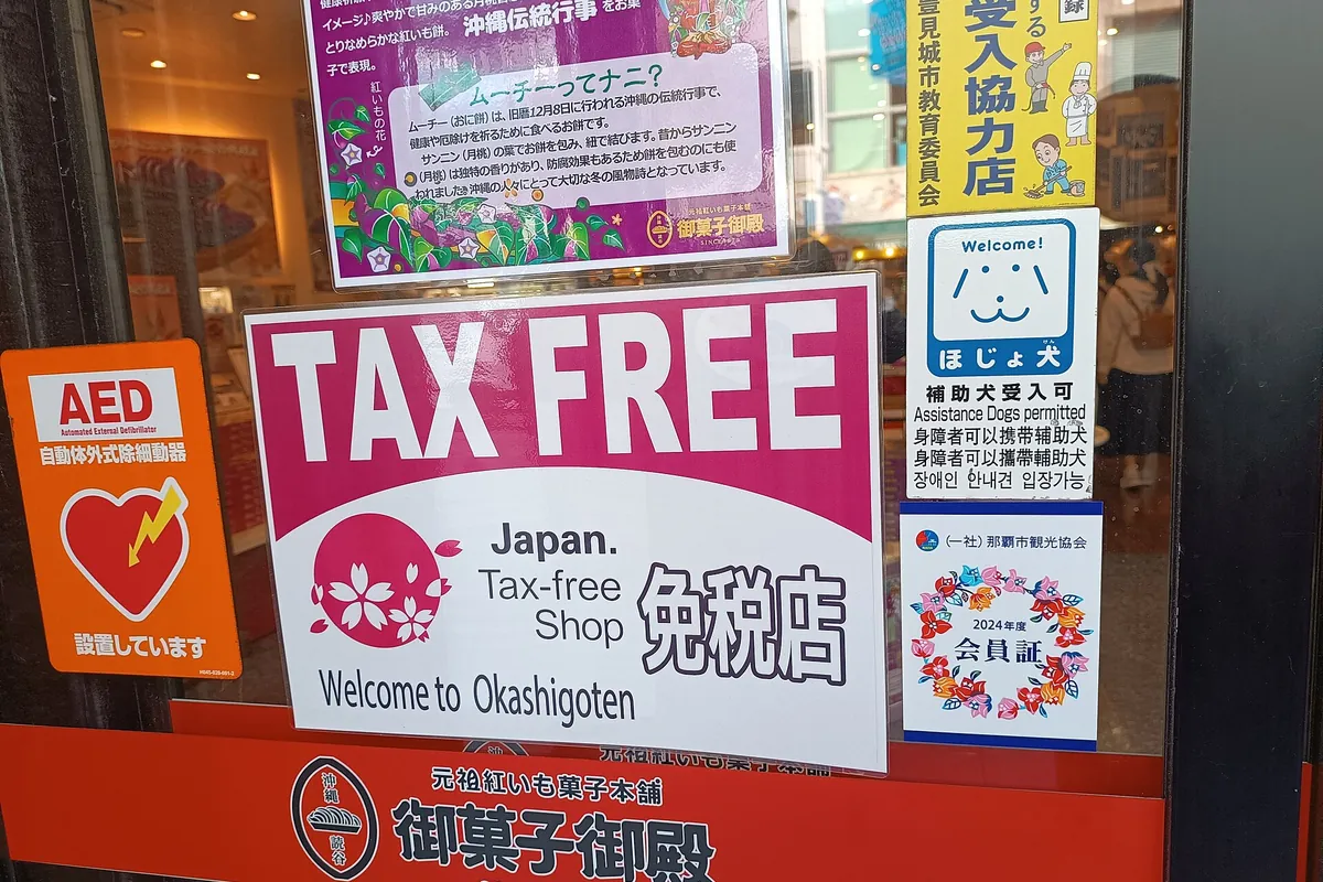 Tax Free sign in a shop window at Okashigoten in Naha, Okinawa, next to an AED sign and an Assistance Dogs permitted sign