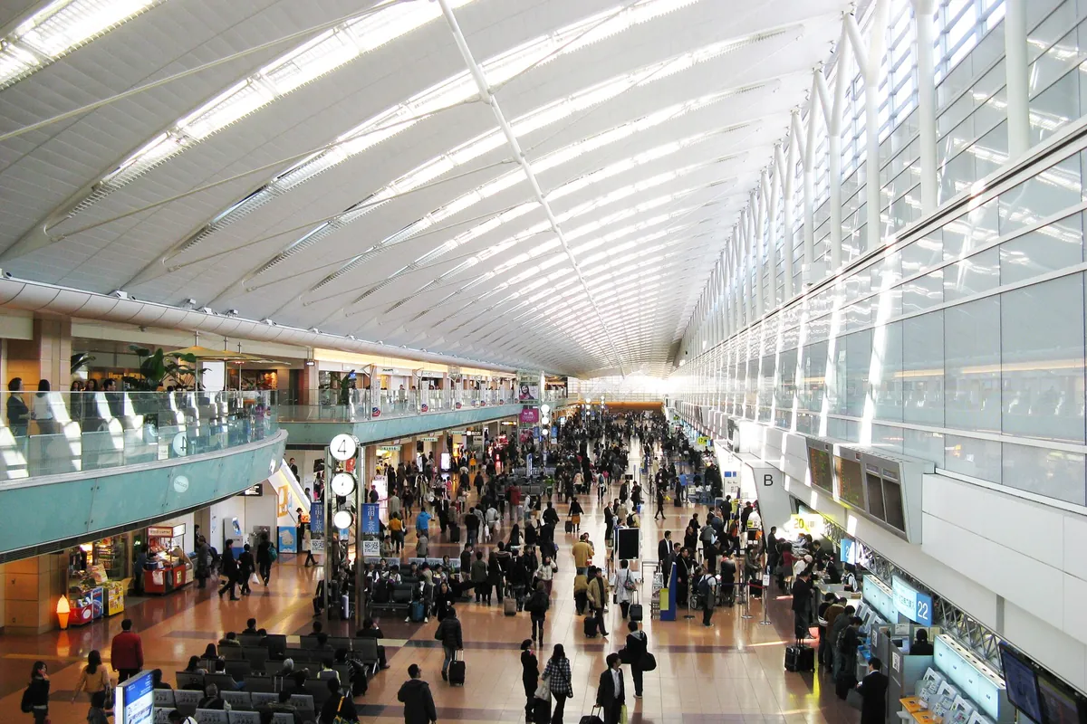 Crowded departure concourse at Haneda Airport with a long curved ceiling and rows of skylights above busy walkways