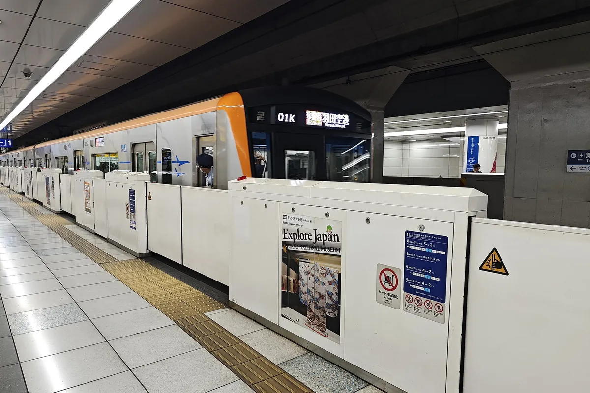 An orange and white Keikyu Line train with a Haneda Airport destination sign at a platform in Haneda Airport Terminal 3 stati