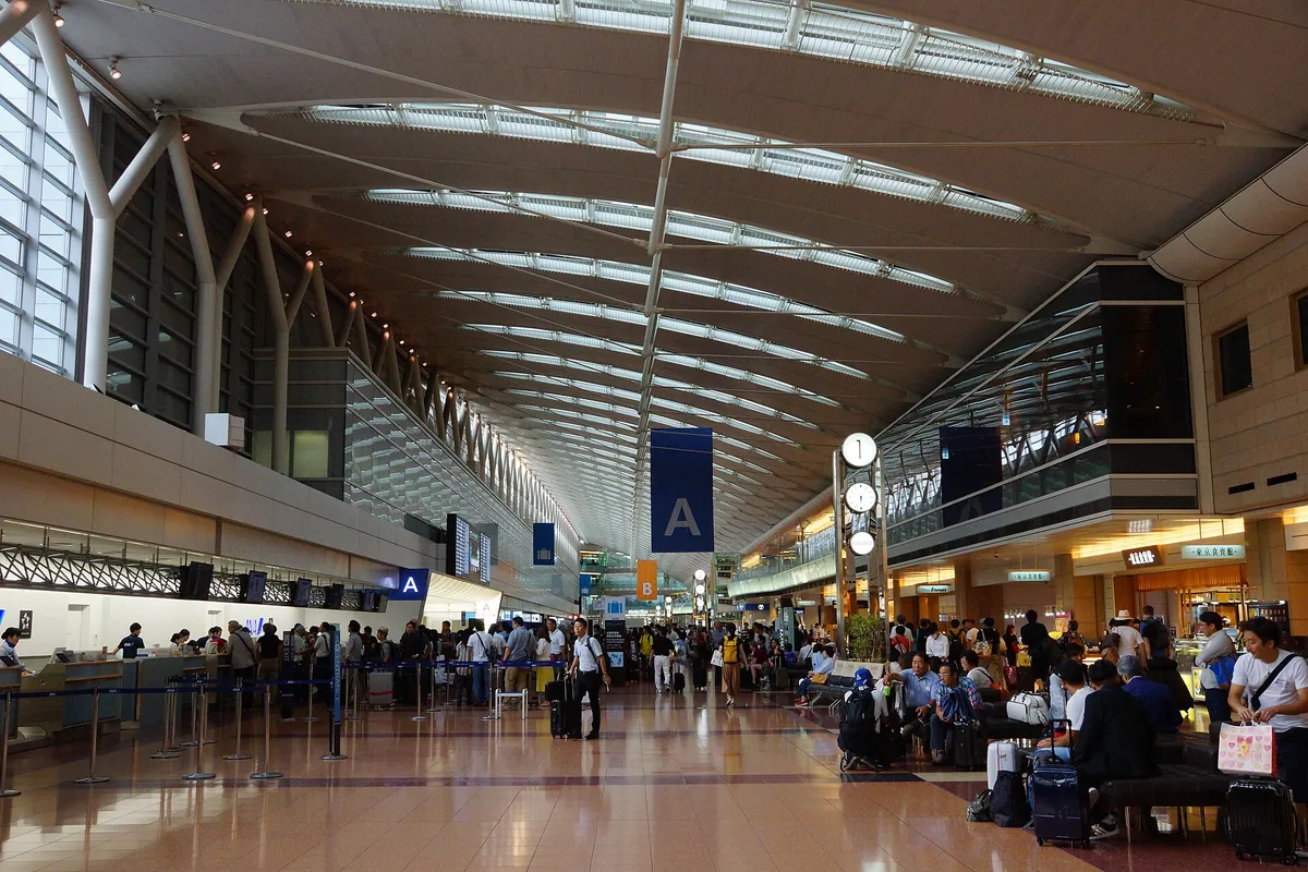 Check-in counters and a wide departure hall with a curved ceiling at Haneda Airport, crowded with travelers and luggage