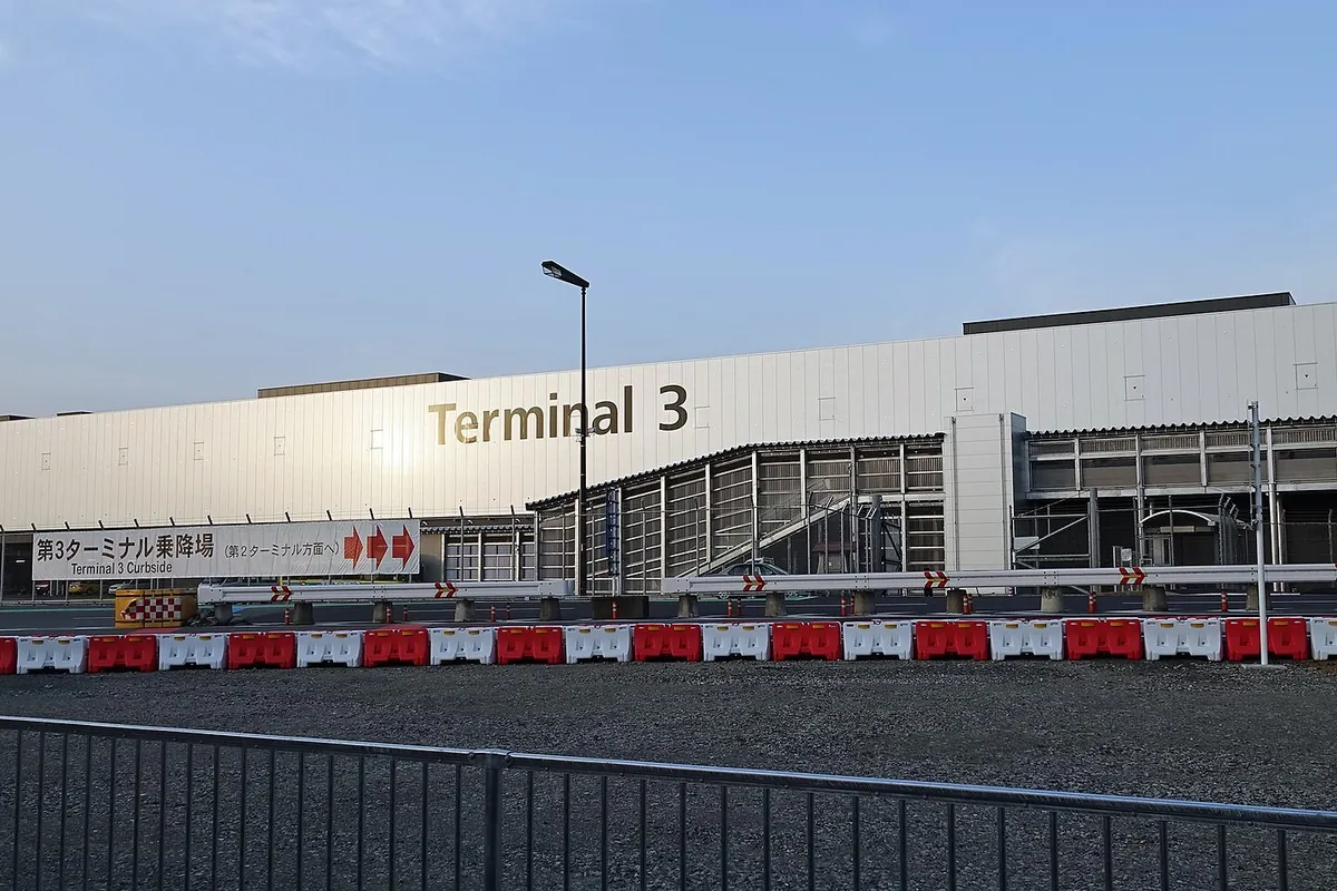 Exterior of the Narita International Airport Terminal 3 building with a Terminal 3 sign and curbside barriers
