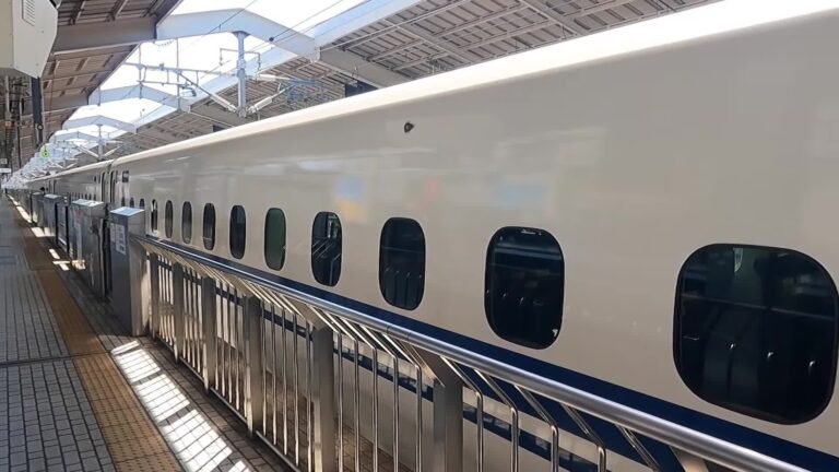 A white Tokaido Shinkansen train with a blue stripe alongside a platform at Kyoto Station
