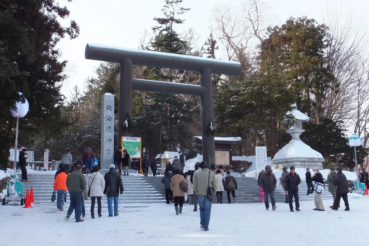雪に覆われた北海道神宮の大きな黒い鳥居と、参道脇の石灯籠